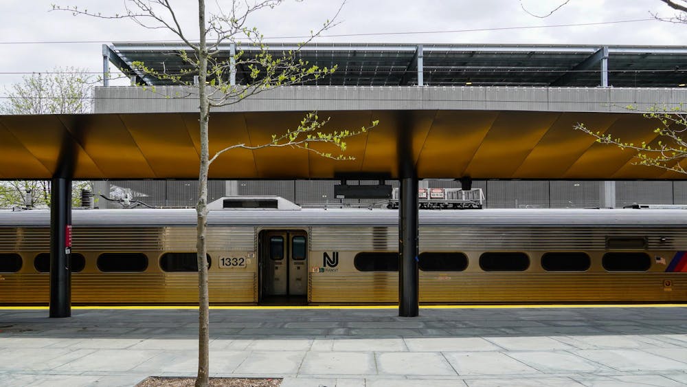 A silver train with a stone pavement ground and one small tree with little leaves.