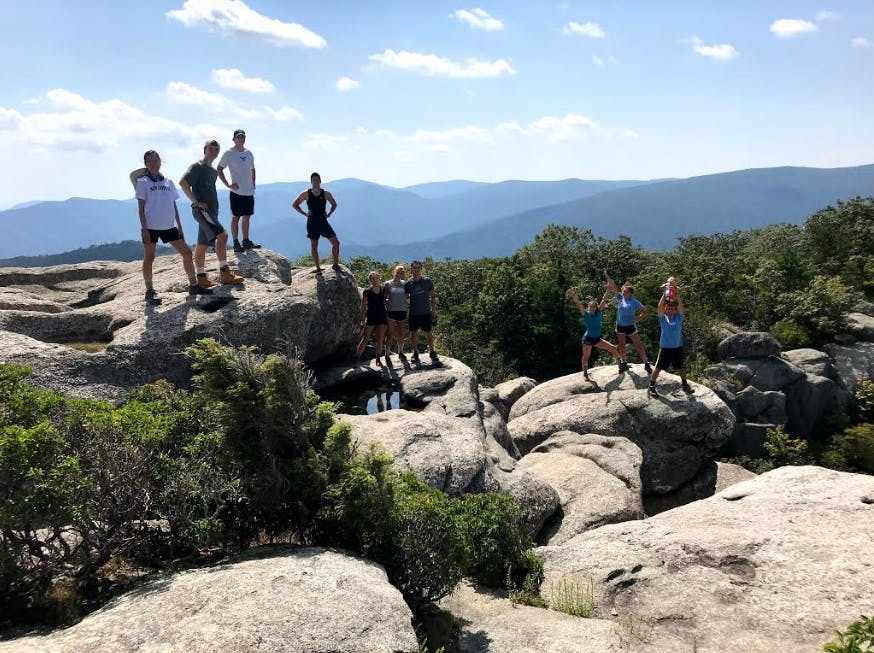 Students stand atop a rock in front of mountains. 