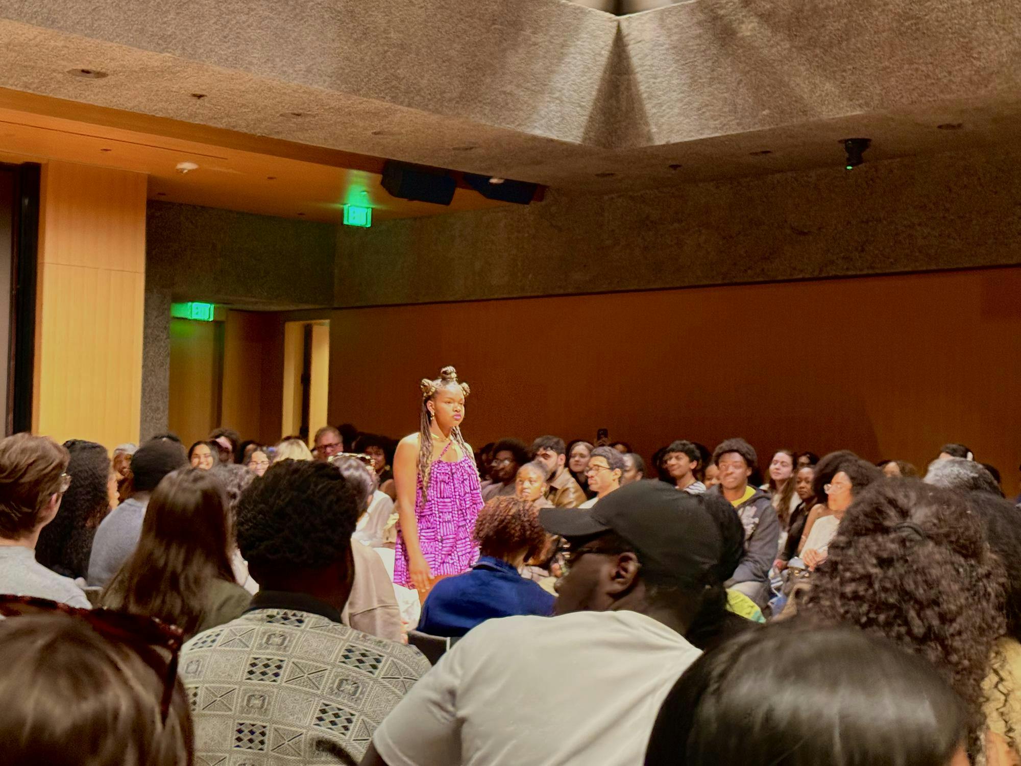 Model on the runway dressed in a pink dress among a crowd of Sankofa attendees. 