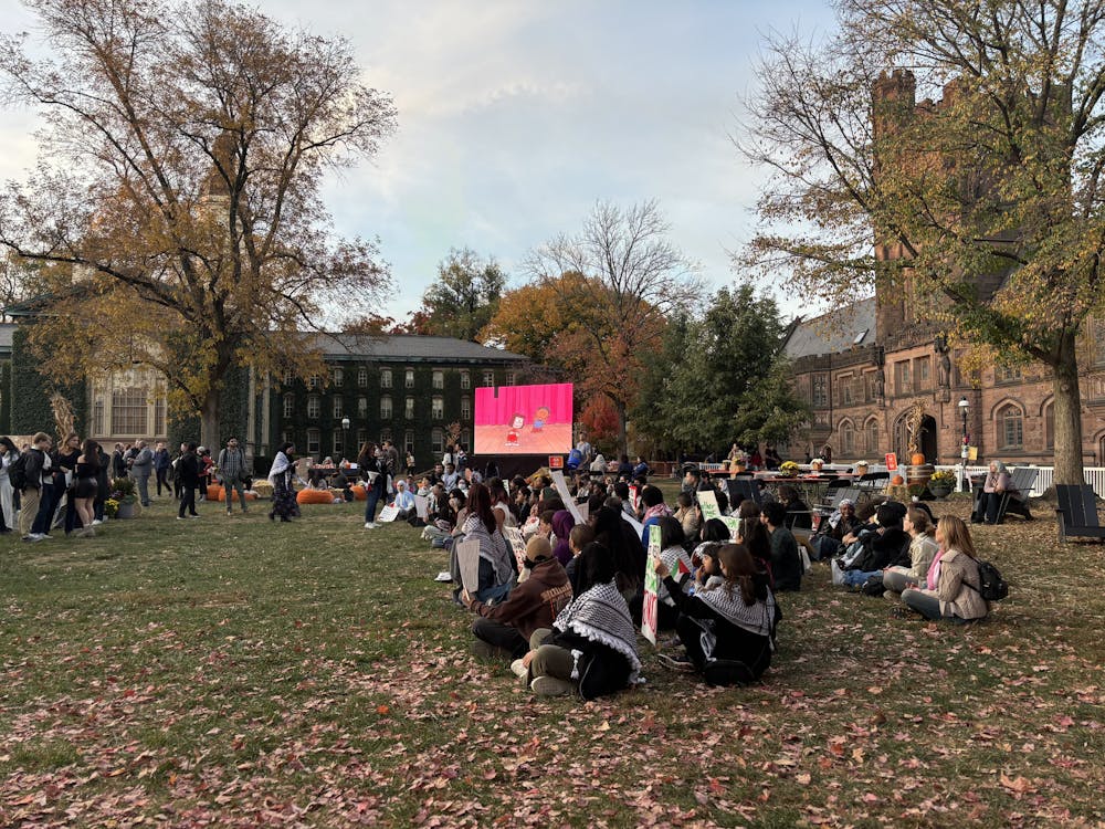 A group on people sit on a lawn, with a projector playing a cartoon behind them