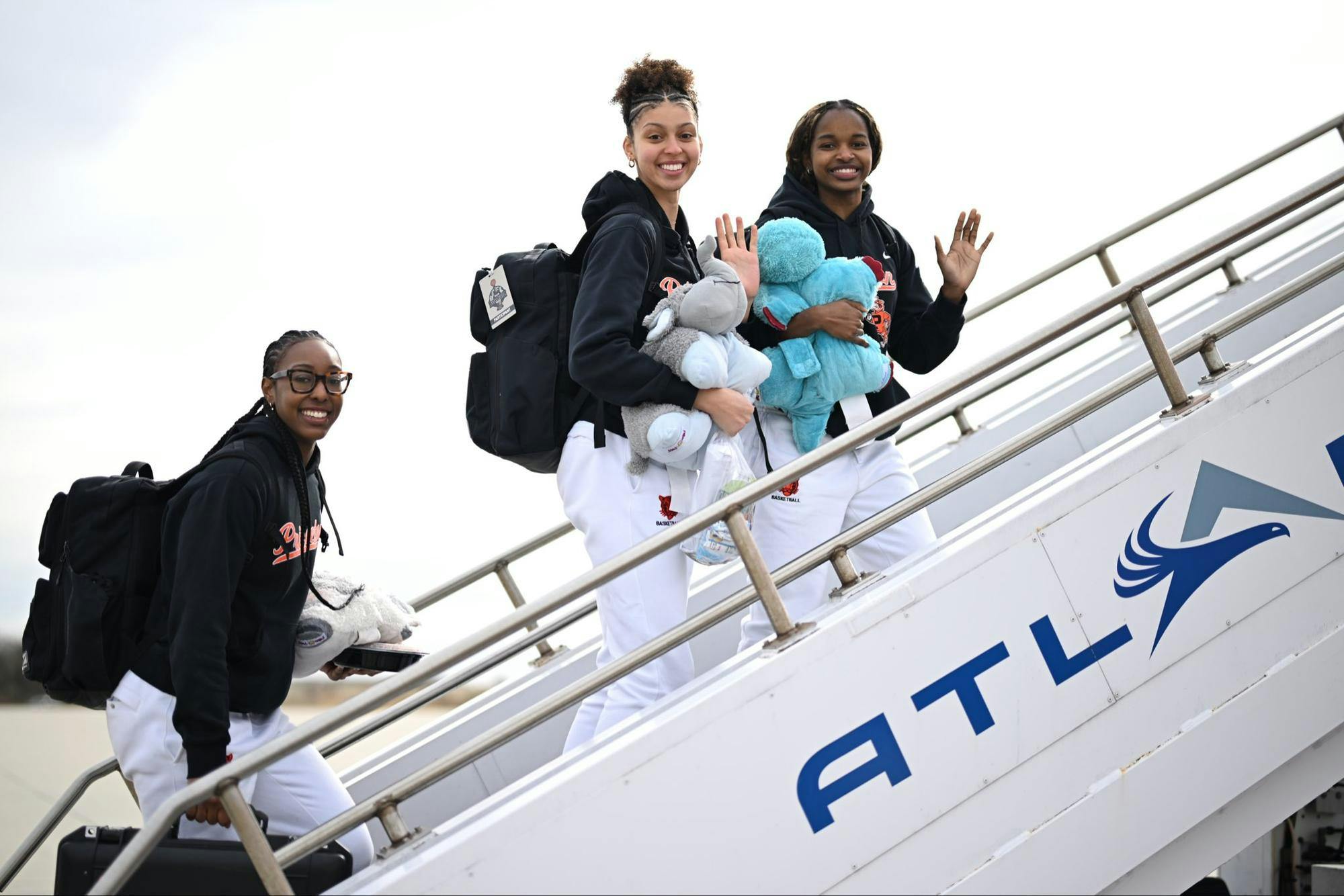 Three people in black sweaters and white sweatpants walk up the stairs to a plane