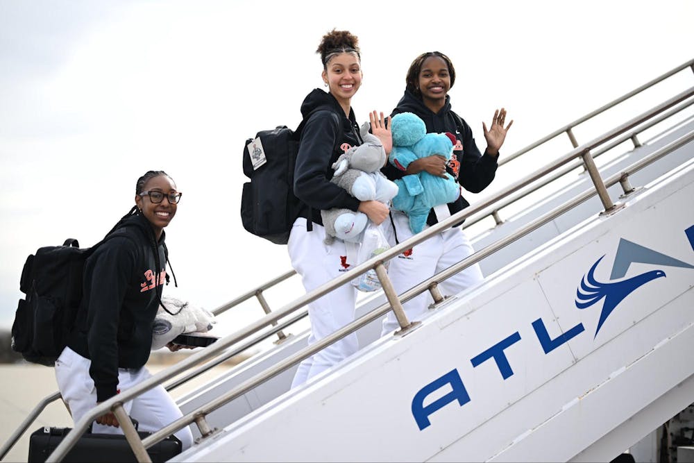 Three people in black sweaters and white sweatpants walk up the stairs to a plane