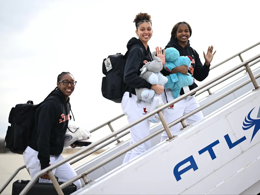 Three people in black sweaters and white sweatpants walk up the stairs to a plane