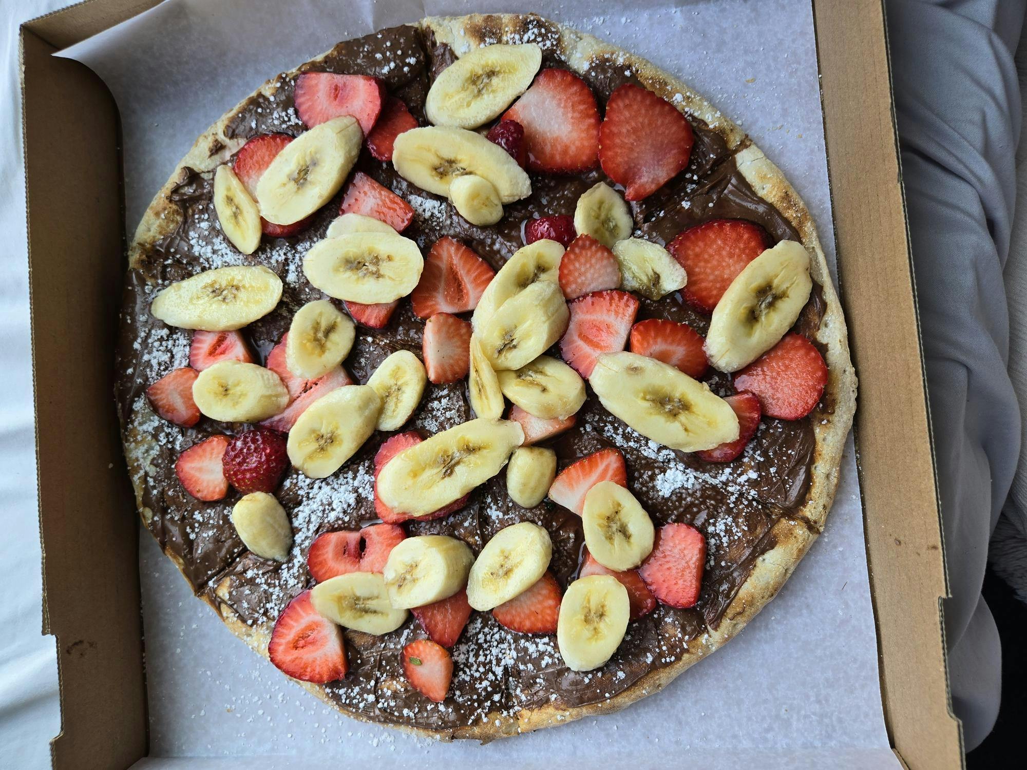 A pizza covered in Nutella, strawberries, and banana.