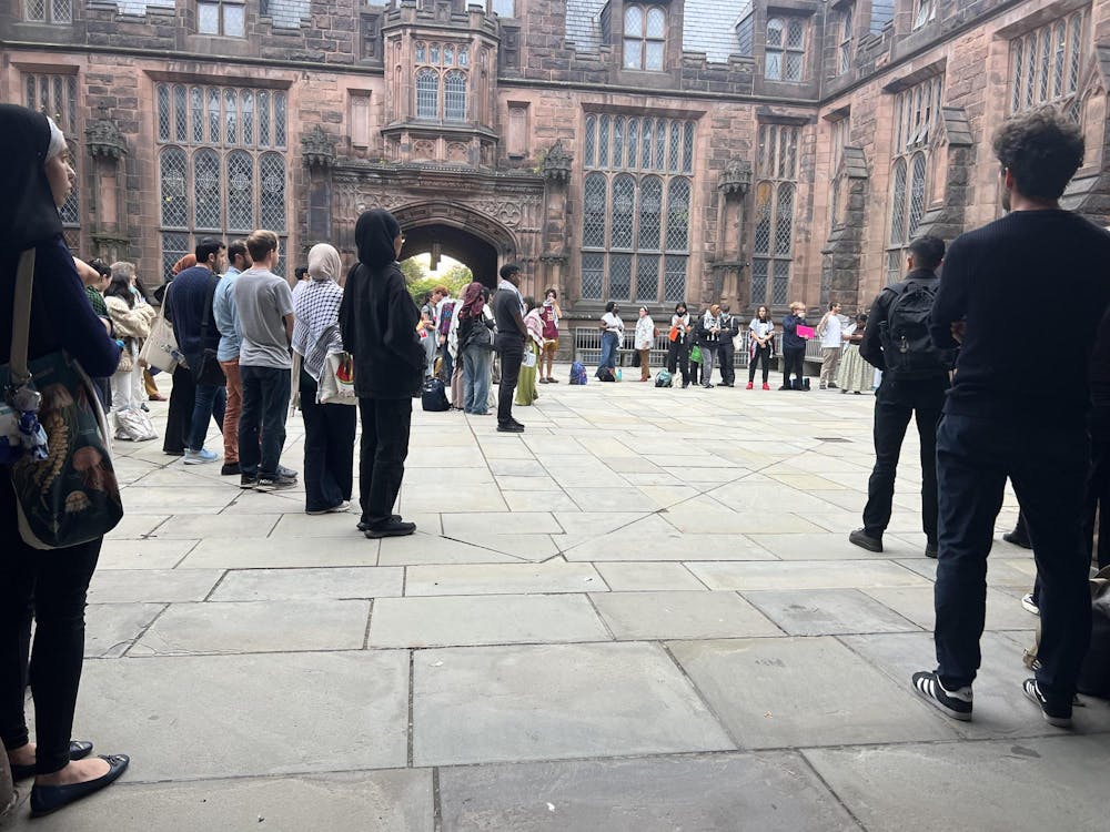 A group of people stand in a large circle in a stone courtyard. 