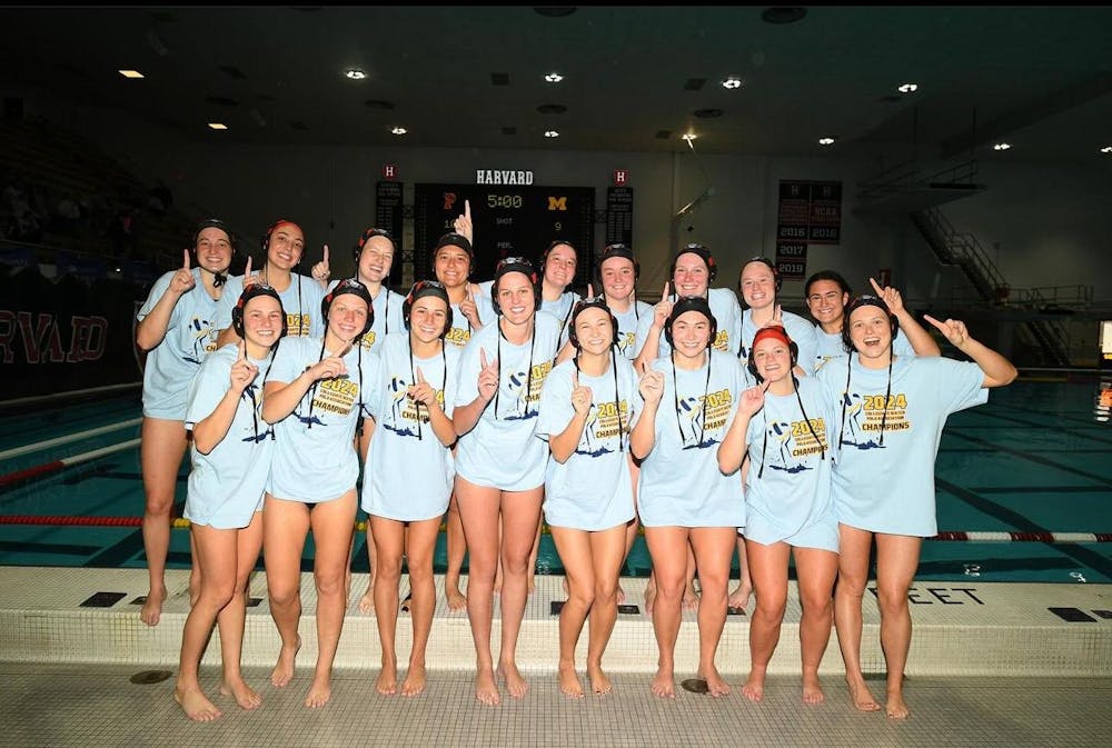 A group of women pose in front of a pool wearing the same shirt holding up the number one sign.