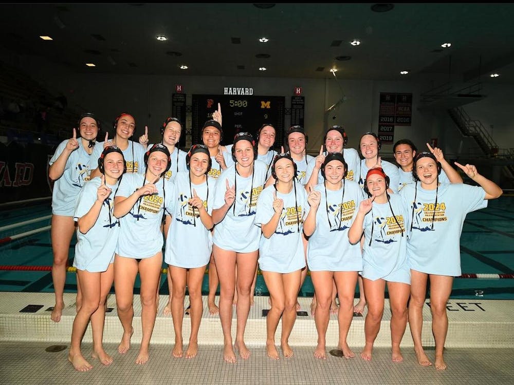A group of women pose in front of a pool wearing the same shirt holding up the number one sign.