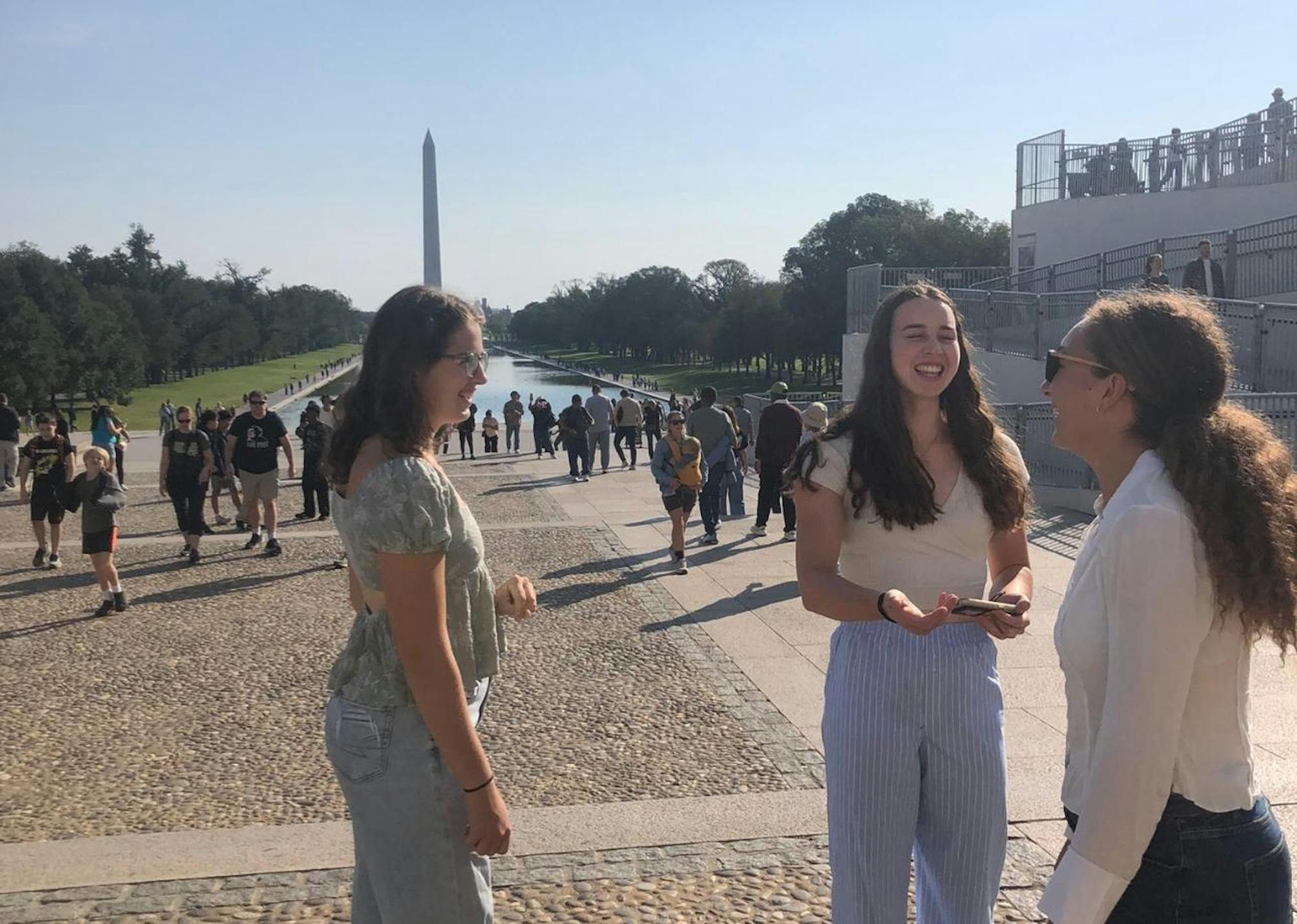 Three women talking in front of the Washington Monument as one prepares to record a video. 