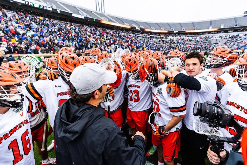 Princeton men’s lacrosse players huddle together on the field after a game, surrounded by fans in a stadium.