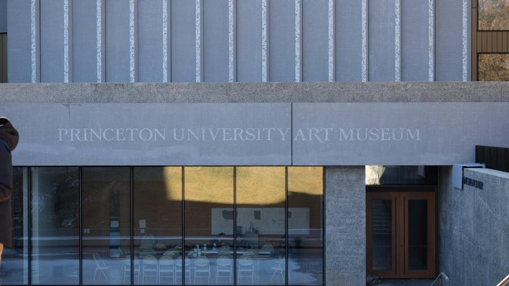 The front of a grey building with the building name "Princeton University Art Museum" plastered above floor-to-ceiling windows and the entryway 