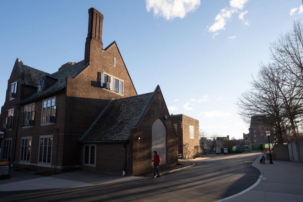 A stone building is illuminated by the sunrise as a student in a red jacket walks by.