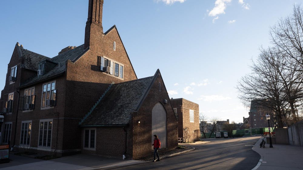A stone building is illuminated by the sunrise as a student in a red jacket walks by.
