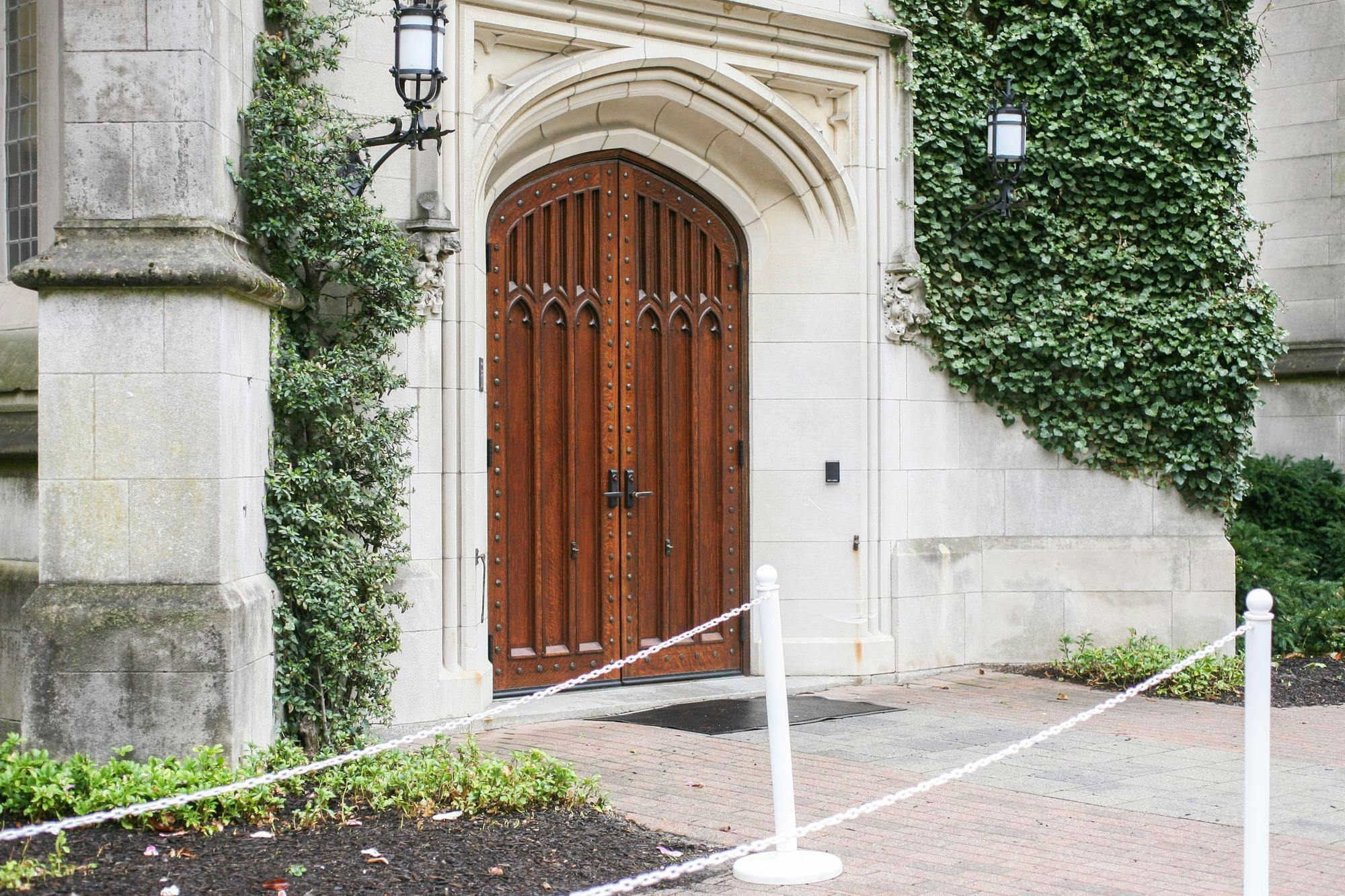 Wooden door on a grey stone, gothic building with greenery growing on its walls.