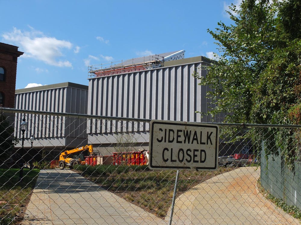 White sign on a fence, with inside there being a construction site of a large grey building.