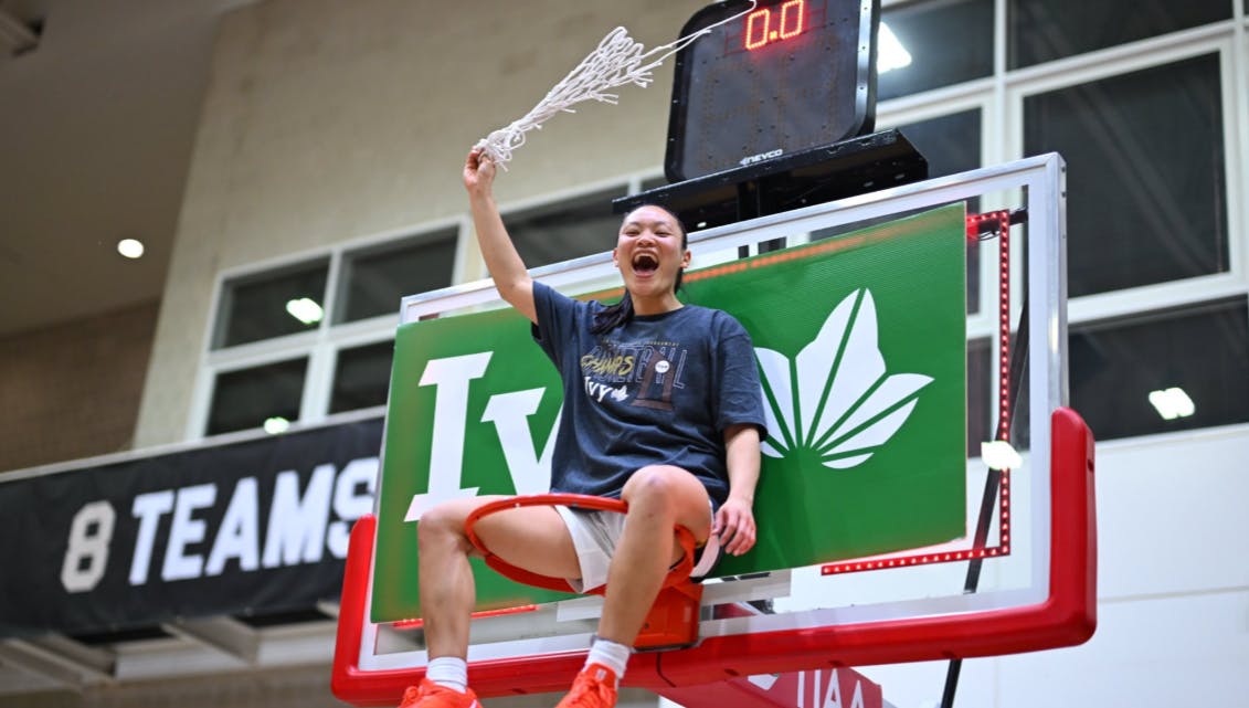 Ashley Chea sitting on a basketball rim.