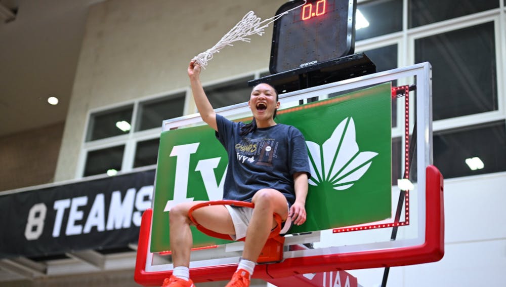 Ashley Chea sitting on a basketball rim.