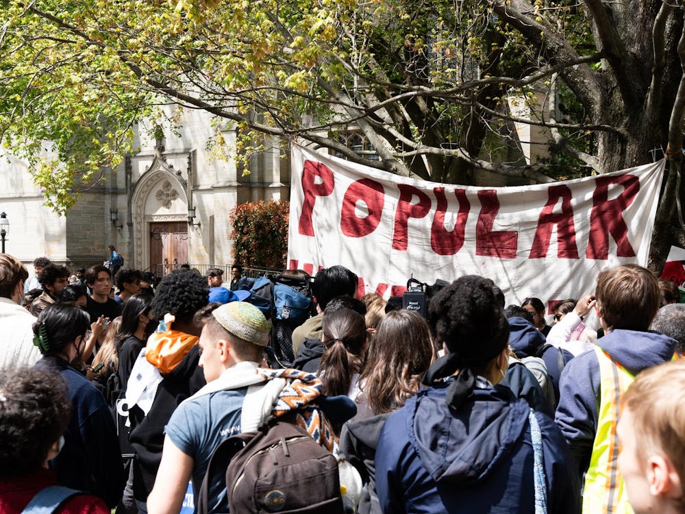 A group of students standing in McCosh courtyard facing a side door of the University Chapel, in front of a white sign hanging from a tree where the word "Popular" is written in all-capital red letters.