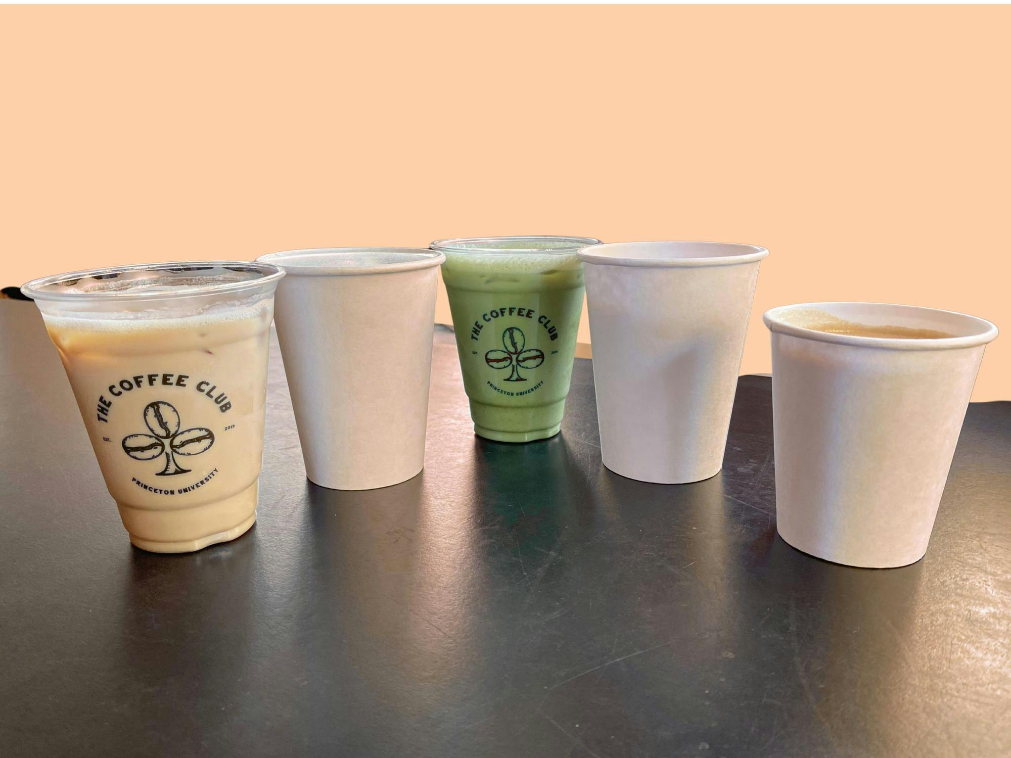 Five drinks sit on a table against a light orange background. 
