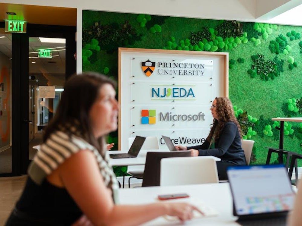 Enfocó en una mujer trabajando en su computadora, sentada enfrente de un signo del “AI Hub Founding Partners”.