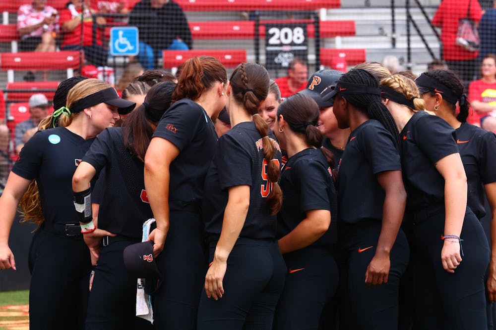 Group of women in black shirts with orange lettering in a circle in front of red bleachers.
