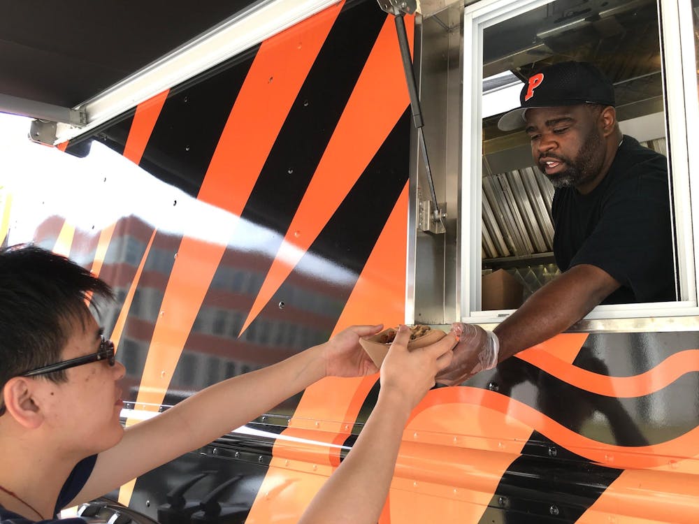 A campus dining worker hands a student some food from the orange and black-colored campus food trucks. 