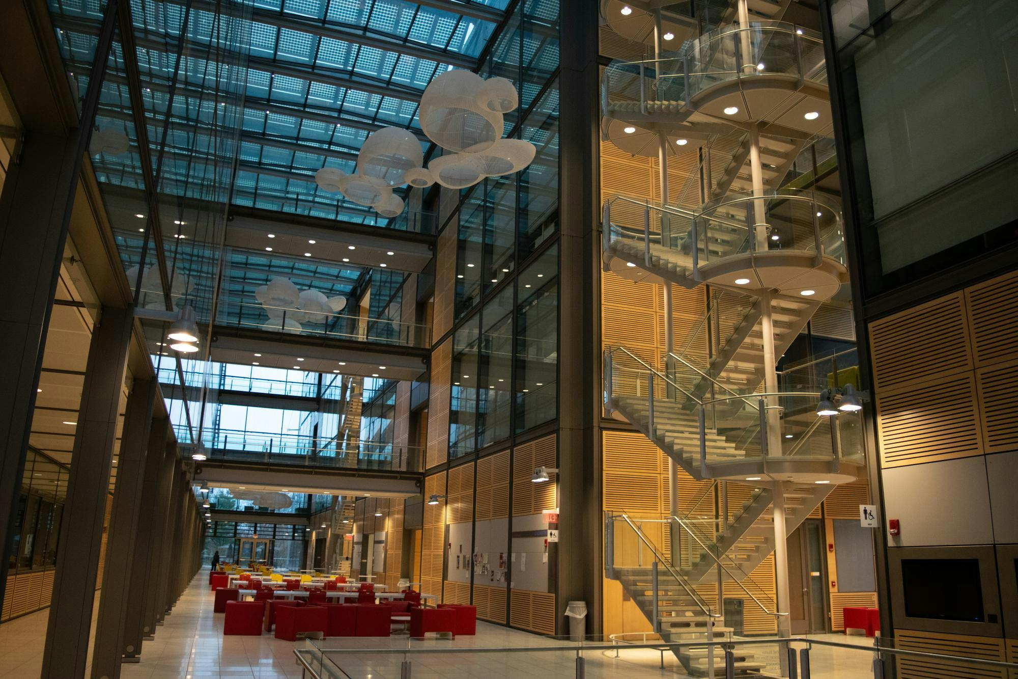 The interior of glass building with floating cloud-like lights and stairs to the right.