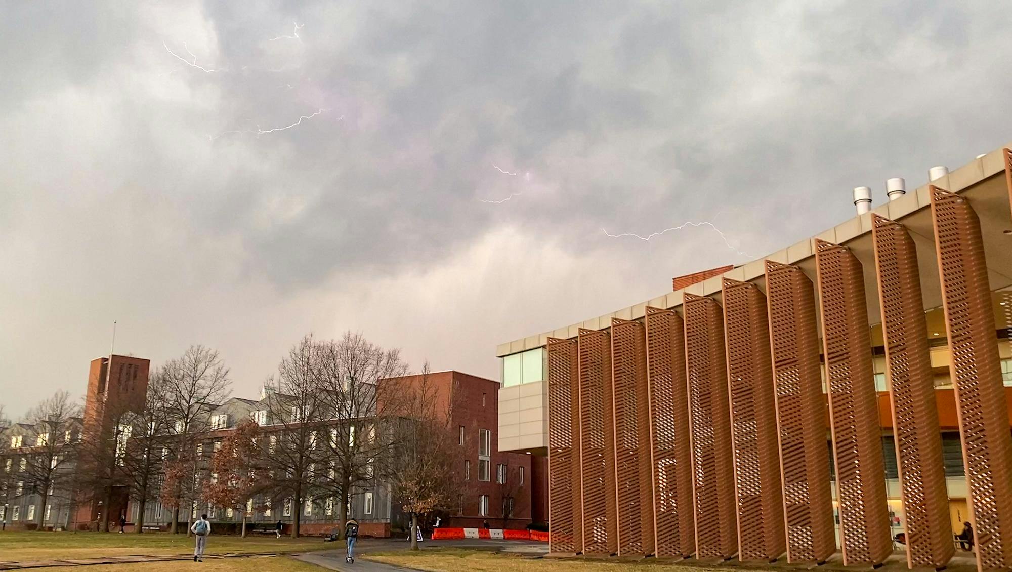 Two buildings are behind a field. There is lightning in the sky.