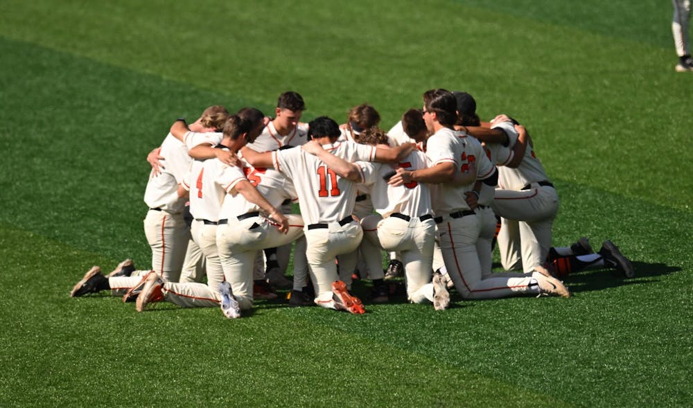 A group of men huddling around on one knee on a baseball field. 