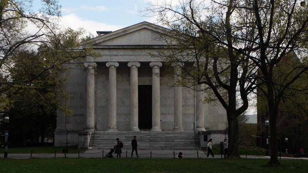A white columned building with a lawn of grass in front and trees.