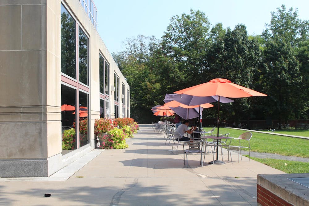 Bright glass building. Behind building is a line of tables and chairs with orange umbrellas at each table.