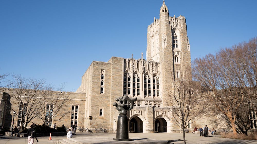 A metal statue is in front of a large stone building with big windows and two arches at its entrance.
