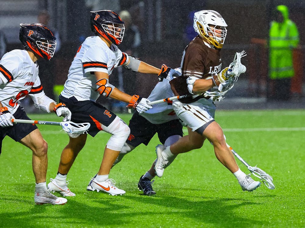 Three lacrosse players in white jerseys surround one in a brown jersey.