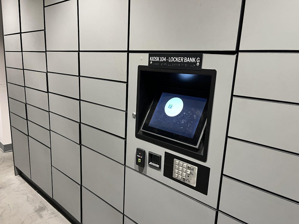 Grey locked cubbies with large black kiosk in the center with a screen.