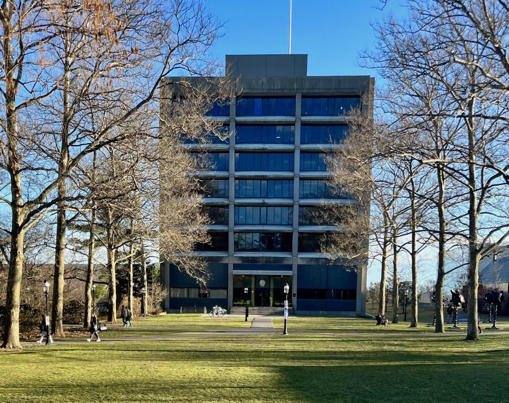 Large glass and concrete building eight stories tall (New South) in center. Surrounded by leafless trees on either side.