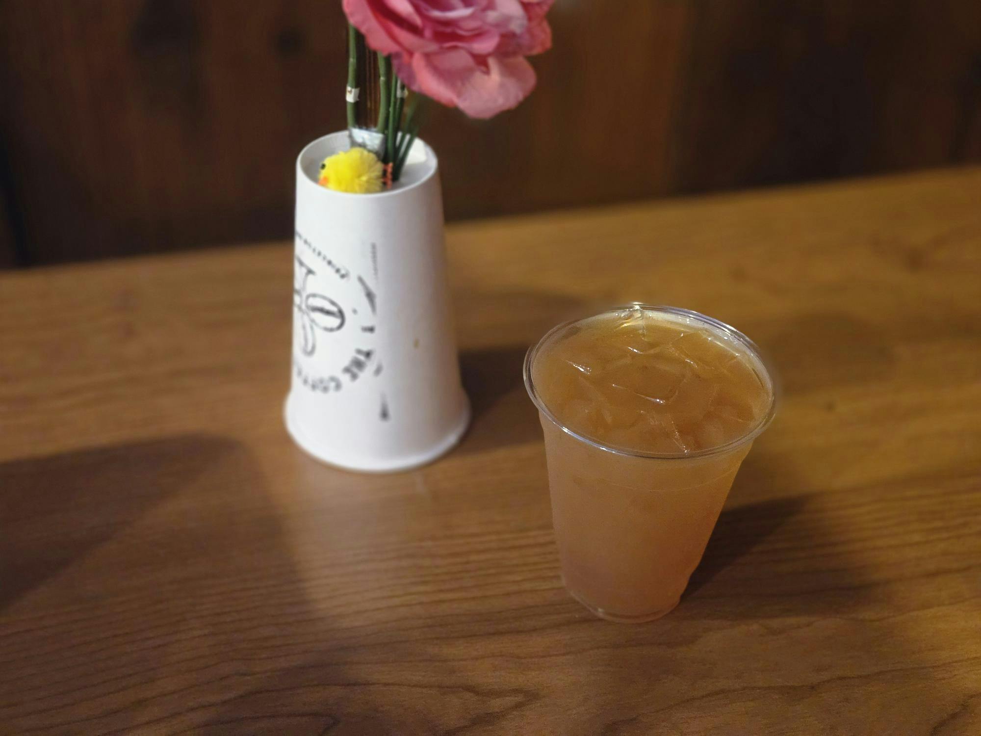 A light orange drink in a transparent cup and a white upside down Coffee Club cup sit on a brown table.