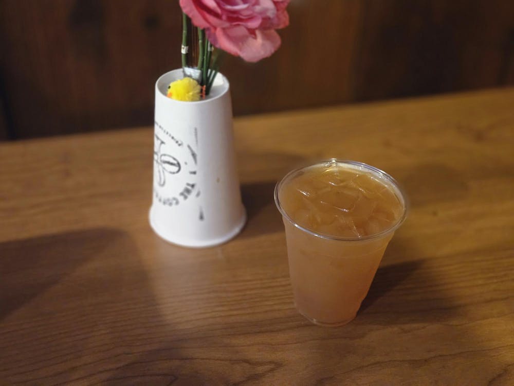 A light orange drink in a transparent cup and a white upside down Coffee Club cup sit on a brown table.