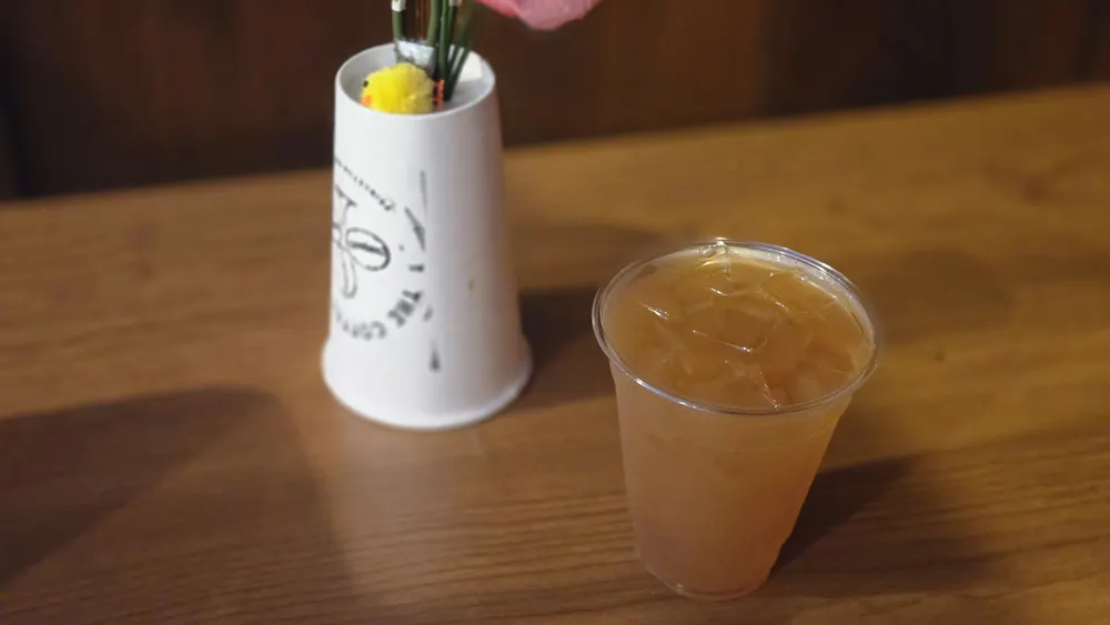 A light orange drink in a transparent cup and a white upside down Coffee Club cup sit on a brown table.
