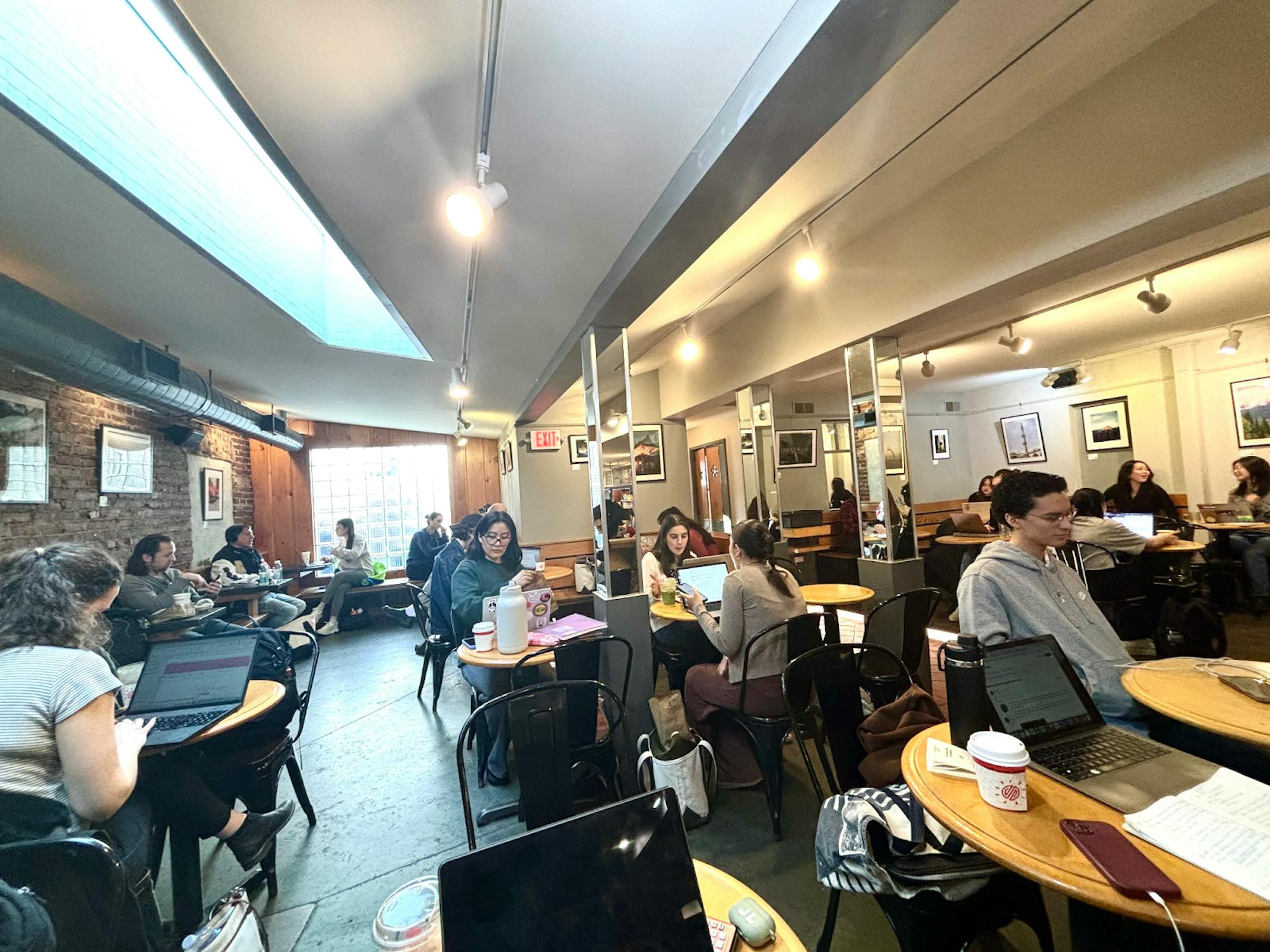 Many tables in the back of a coffee shop are occupied by students doing their work and conversing with each other. 