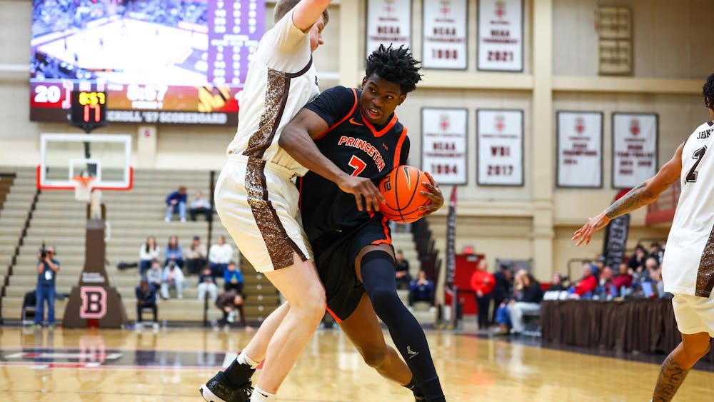 Player in a black and orange jersey drives toward the basket while being defended by a Brown player.