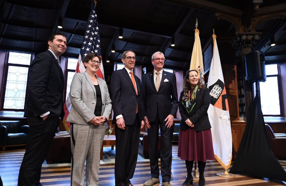 Five people — two women and three men — stand in front of a podium and flags, smiling for a photo.