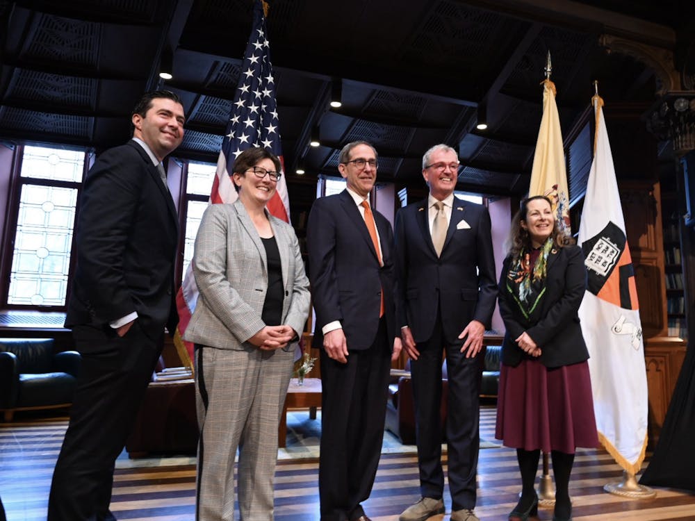 Five people — two women and three men — stand in front of a podium and flags, smiling for a photo.