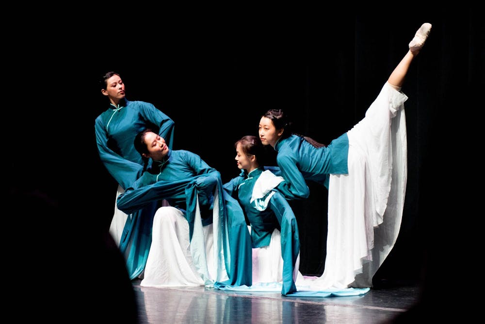 Four dancers in blue and white outfits perform before a black background.