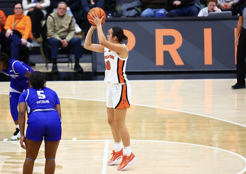 Woman shoots a basketball towards the basket, she is wearing a white Princeton basketball uniform.