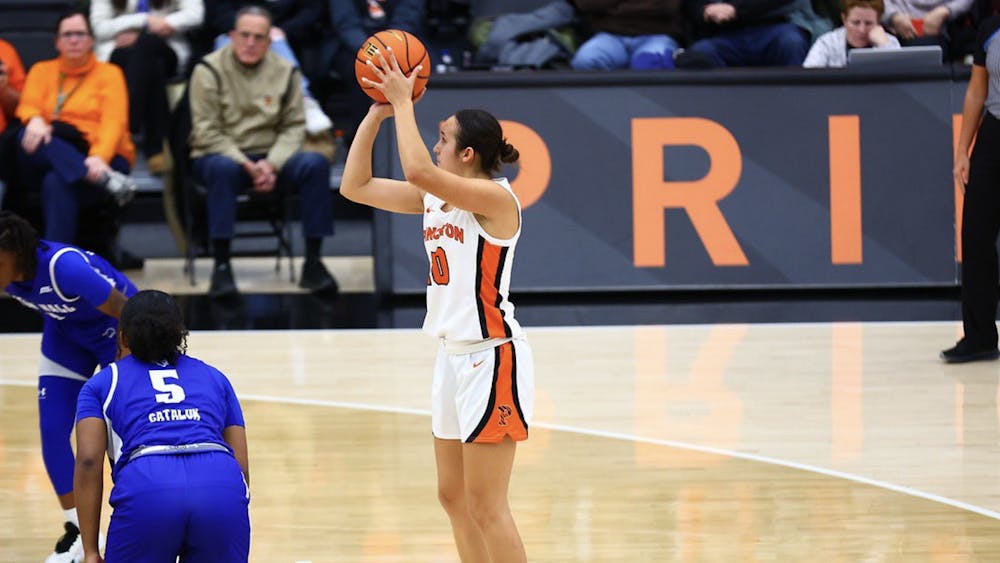 Woman shoots a basketball towards the basket, she is wearing a white Princeton basketball uniform.