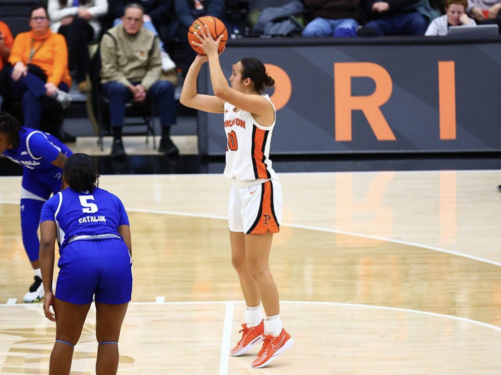Woman shoots a basketball towards the basket, she is wearing a white Princeton basketball uniform.