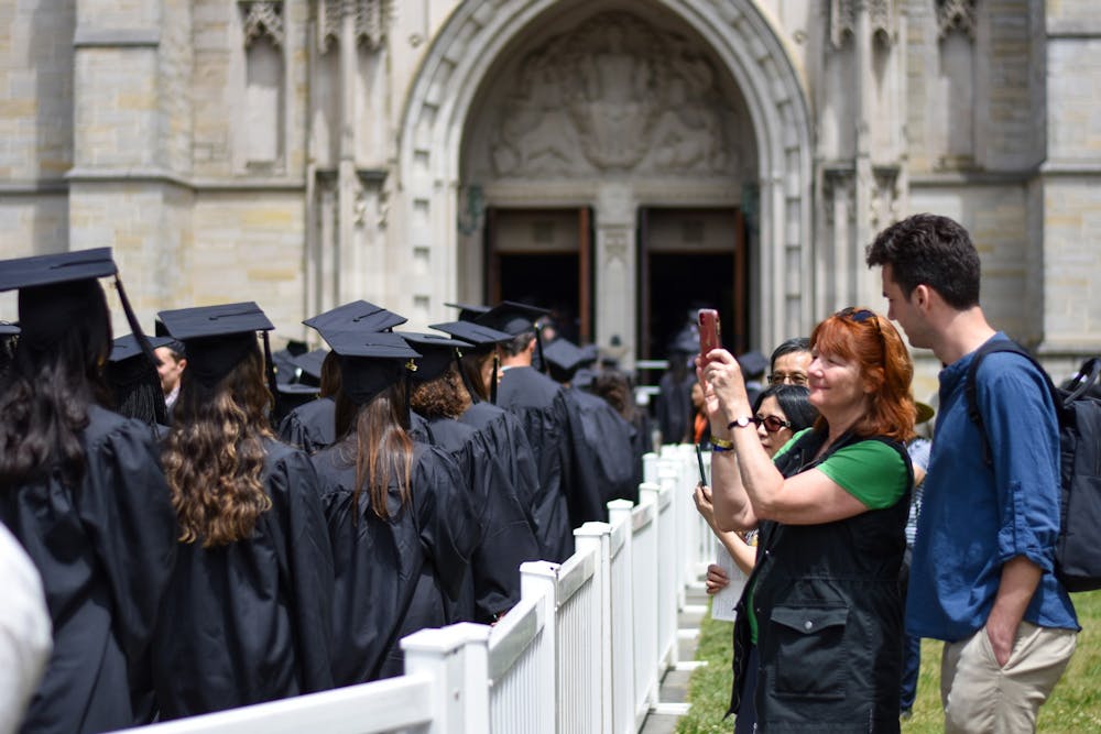 A photo of parents taking pictures of the graduating students clad in black caps and gowns as they walk into the Chapel.
