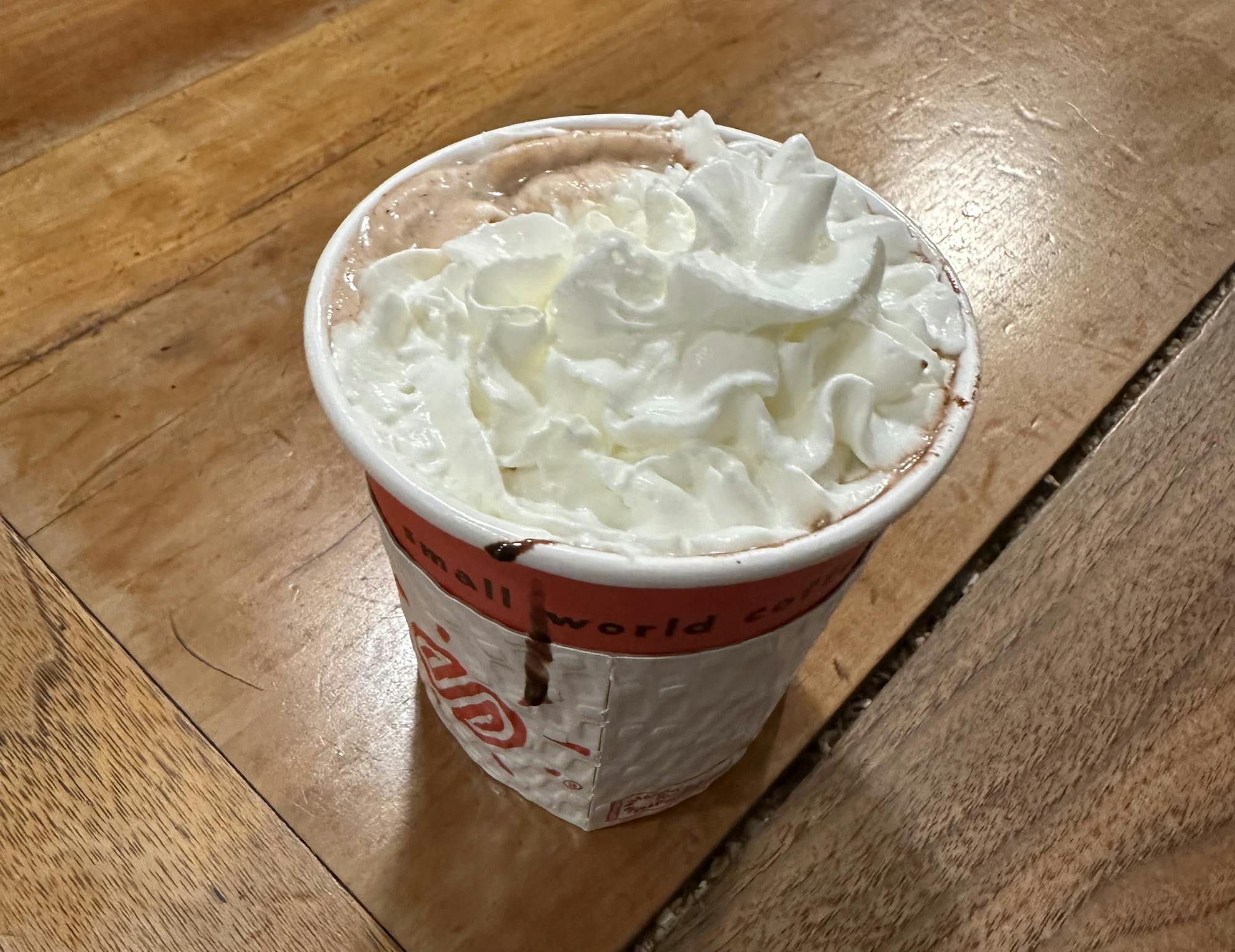 A hot chocolate topped generously with whipped cream sits on a wooden table.