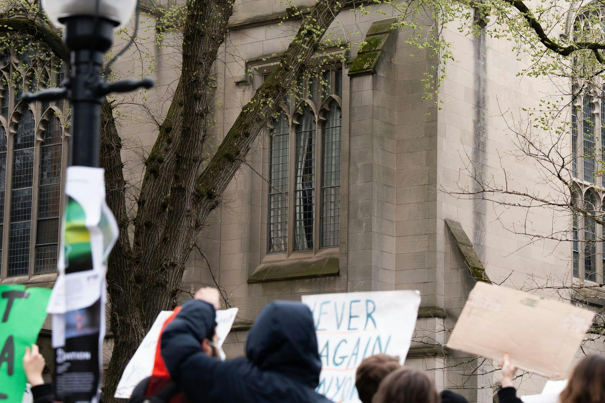 Protester with sign stand outside of McCosh hall as someone peers out of the window. 
