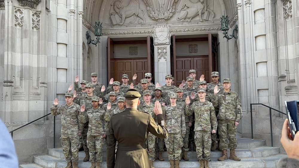 A group of ROTC students dressed in tan and olive green camo uniforms facing a lieutenant colonel, all with their right hands raised for an oath.