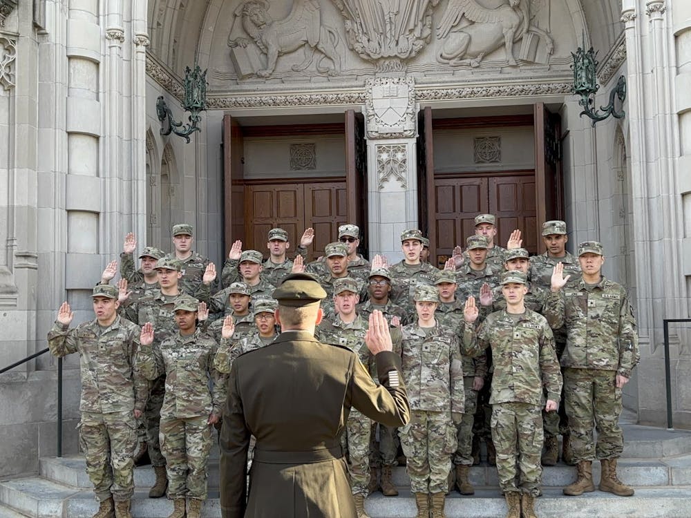 A group of ROTC students dressed in tan and olive green camo uniforms facing a lieutenant colonel, all with their right hands raised for an oath.